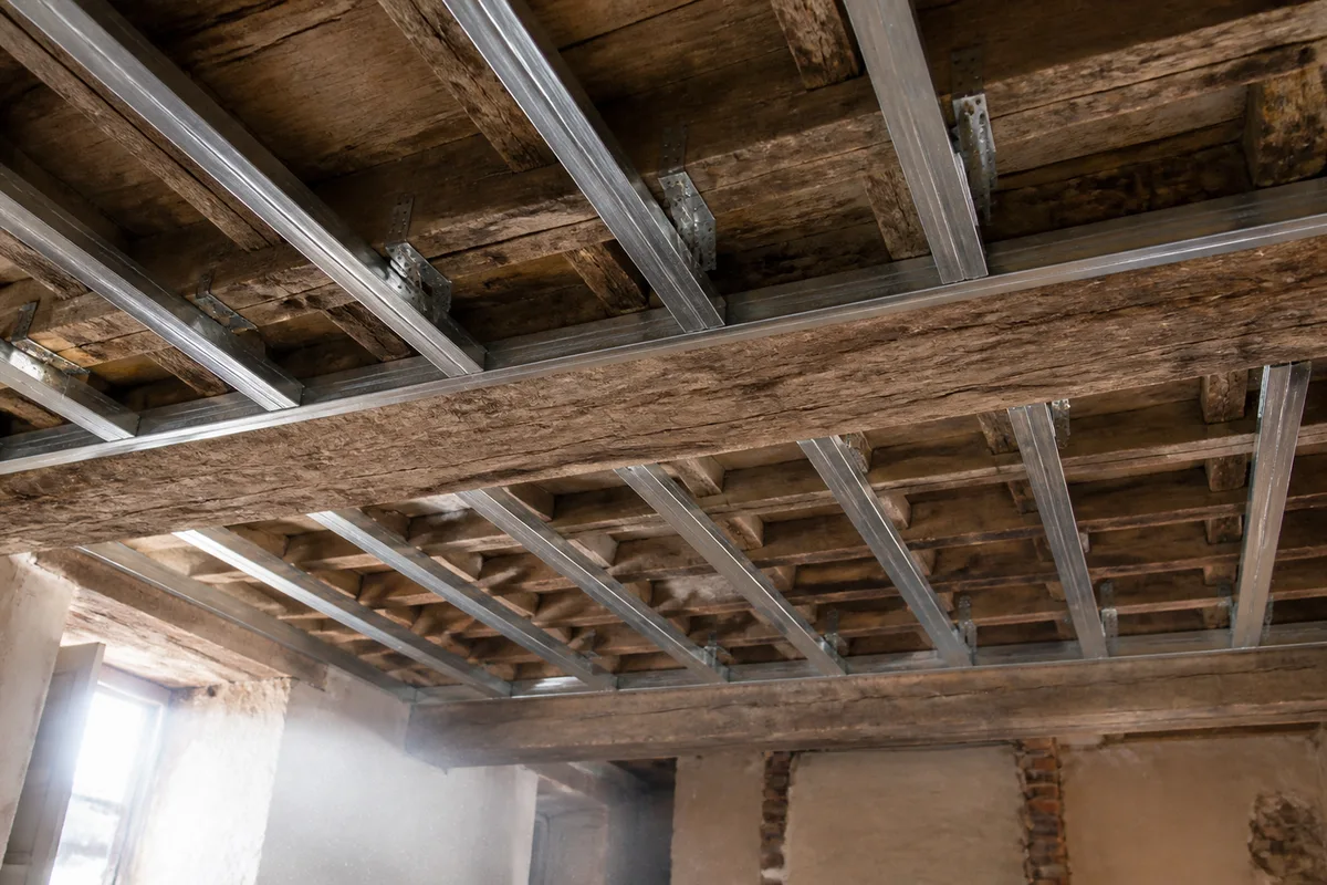 Ossature métallique de plafond, fourrures et suspentes visibles sous une charpente ancienne